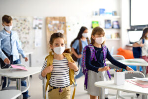 Group of children with face mask back at school after covid-19 quarantine and lockdown, entering classroom.