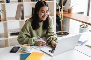 Image of a pretty positive optimistic young girl student using laptop computer indoors studying.