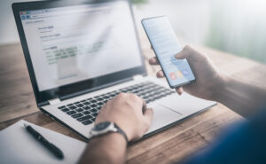 The man works at home and uses a smart phone and a notebook computer. Silhouette of a busy man. One hand holds and uses the phone, the other writes on the laptop keyboard.