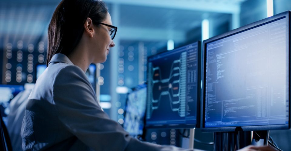 Close-up Shot of Female IT Engineer Working in Monitoring Room. She Works with Multiple Displays.