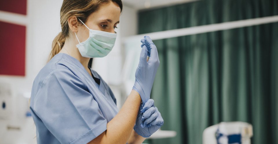 Female nurse with a mask putting on gloves