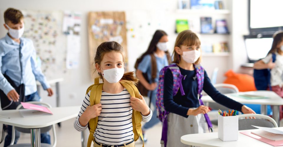 Group of children with face mask back at school after covid-19 quarantine and lockdown, entering classroom.