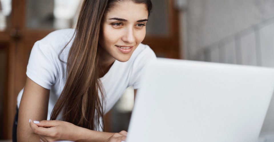 Young female law student using a laptop in public library looking positive smiling. Studying is so much fun. Education concept.