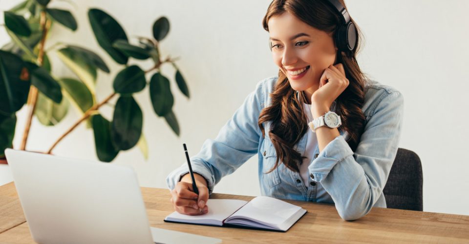 portrait of young smiling woman in headphones taking part in webinar in office