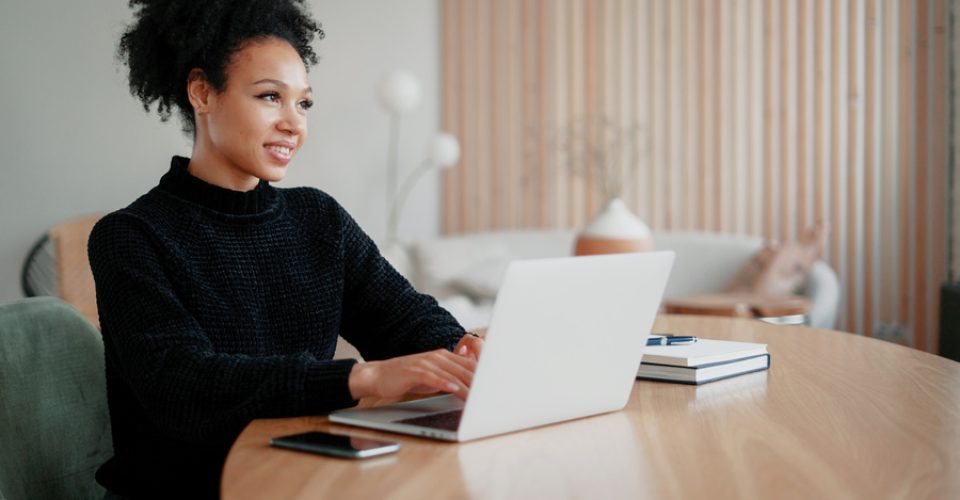 online training is watching videos on a computer gadget. Happy female student freelancer Latin American laughs working in a coworking space. Remote communication with friends.