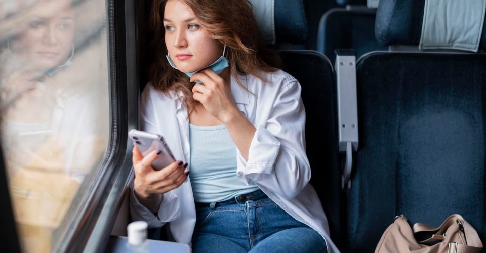 Mulher com máscara médica viajando e usando smartphone. Foto: Imagem de Freepik